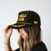 Model adjusting the brim of the black Hot Girls Do Hair trucker hat